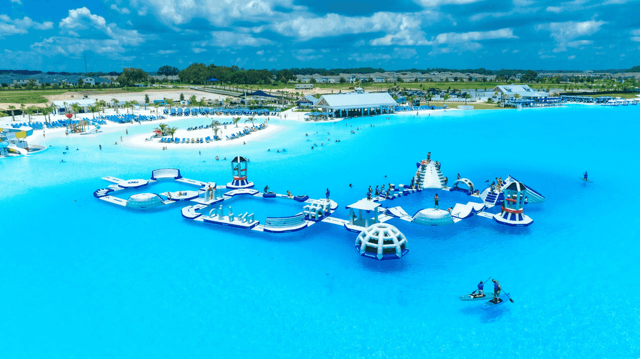 Aerial view of Mirada Lagoon by Metro Development Group, featuring a crystal-clear blue lagoon with floating water park, white sand beach, and surrounding residential community
